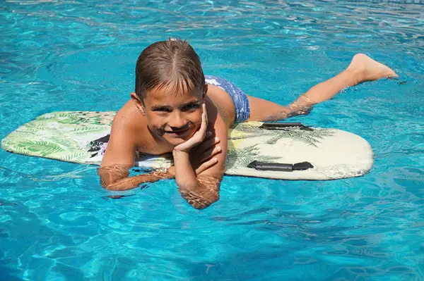 Boy having fun in the pool floating on a pool paddle board.