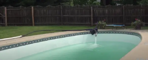 Filling a swimming pool with a large water hose.