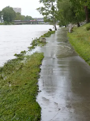 The river is overflowing onto a sidewalk after a heavy rain.