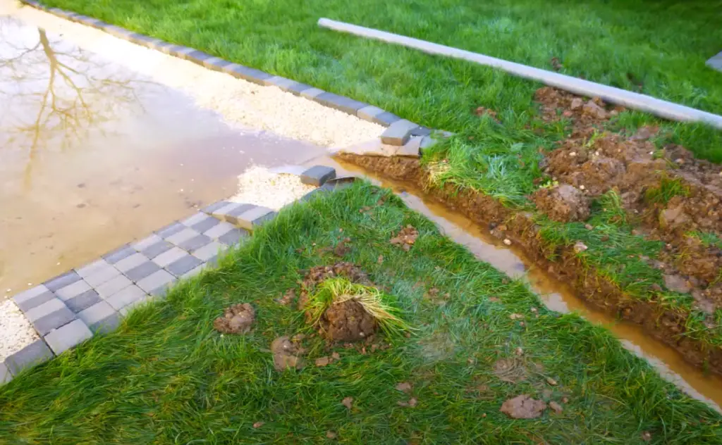 A flooded driveway and French drain trench. Using a French drain system is one of the best sump pump alternatives to keep the house dry and prevent yard flooding.