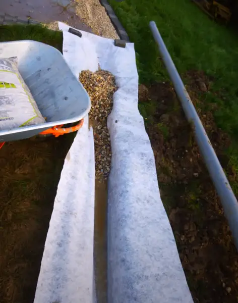 Placing gravel on the landscape cloth in a French drain.