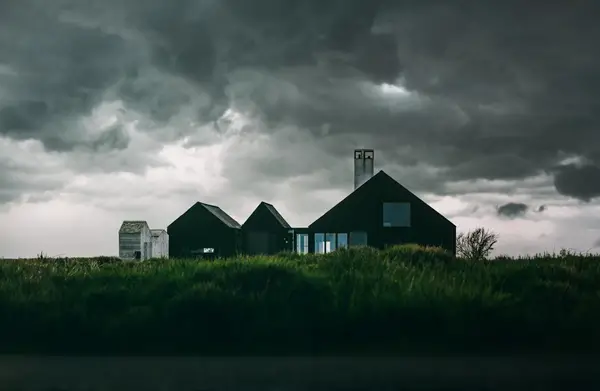 Home and outbuildings under storm clouds. Extreme weather requires all homes to have flood insurance and sump pumps for protection.